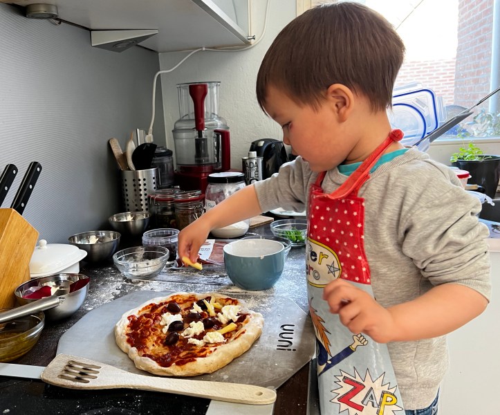 boy putting toppings into a home made pizza